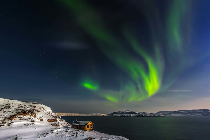 Útulný dům na pobřeží Barentsova moře a polární záře. Poloostrov Kola, Murmanská oblast, Rusko