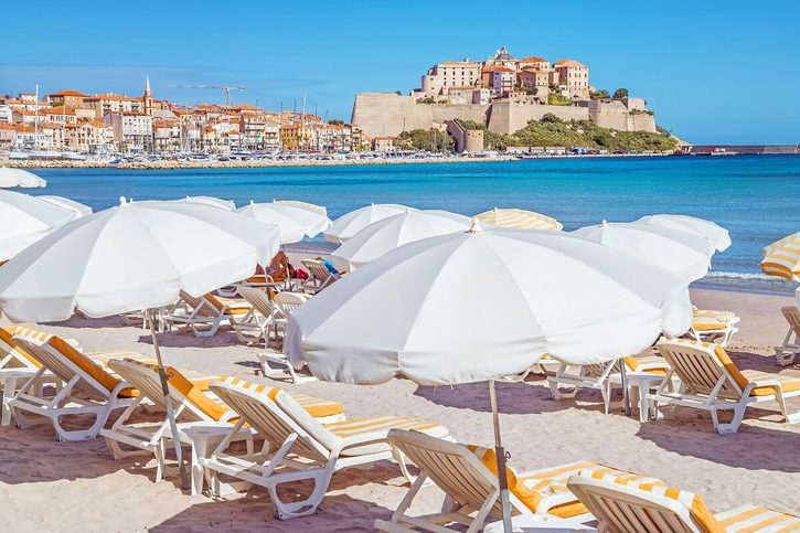 Calvi - Piesočná pláž s tyrkysovým morom a výhľadom na historickú citadelu.
